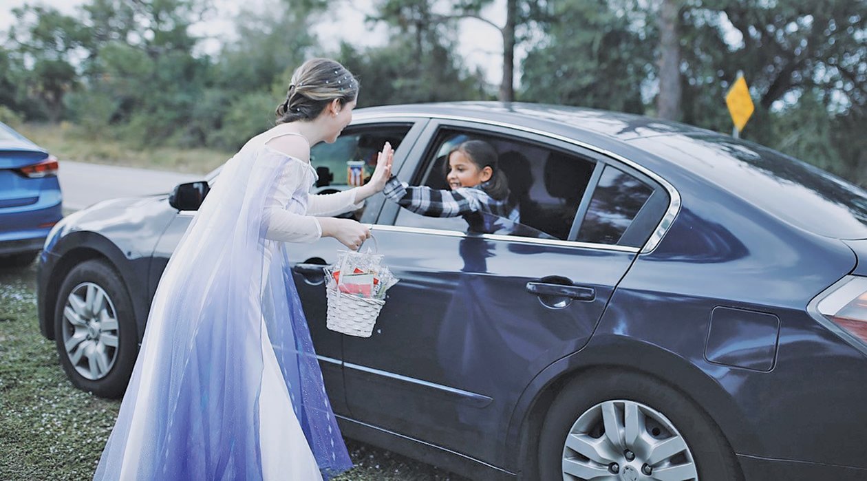 A volunteer dressed as the Disney character Elsa from Frozen (Ms. Marizel Perez, a teacher from Clewiston High school, high giving out candy to a child waiting patiently in her car.